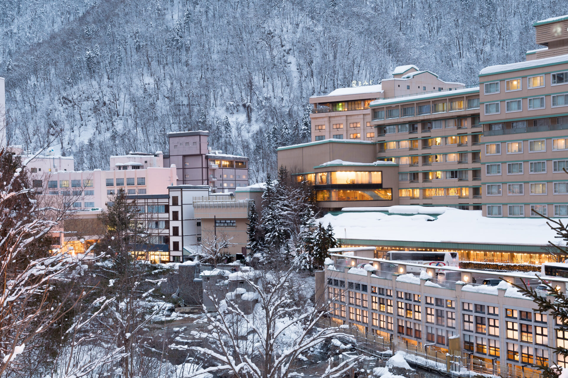 雪山に囲まれた温泉地に立ち並ぶ大型温泉ホテルと、灯りがともる客室や館内の様子